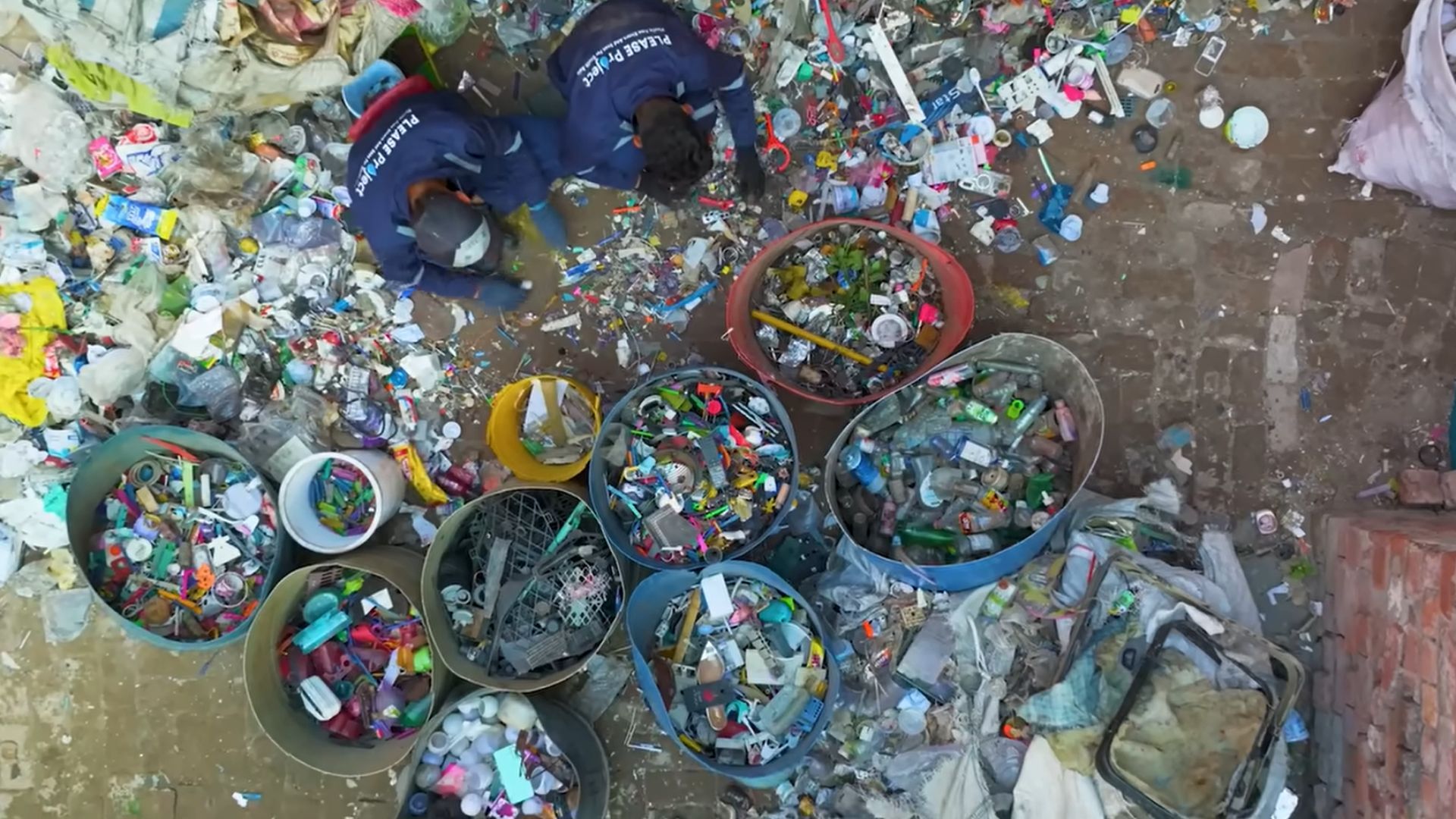 Workers sort mixed plastic waste into large color-coded bins at a recycling facility