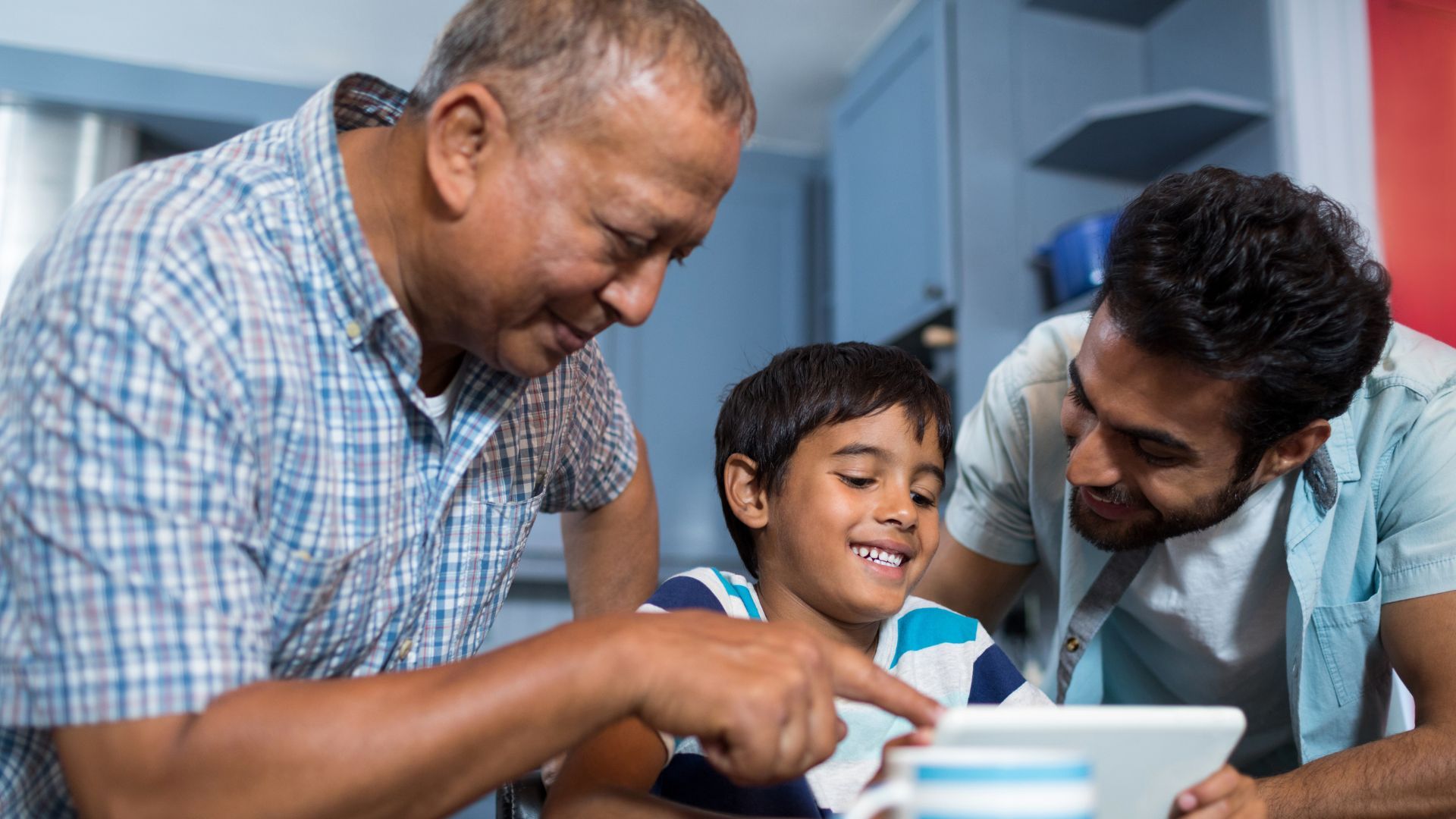 Three people smiling and looking at a tablet together.