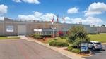 Front entrance of Unilever’s Raeford, USA facility with flagpoles, landscaped grounds and a parked vehicle under a bright blue sky.