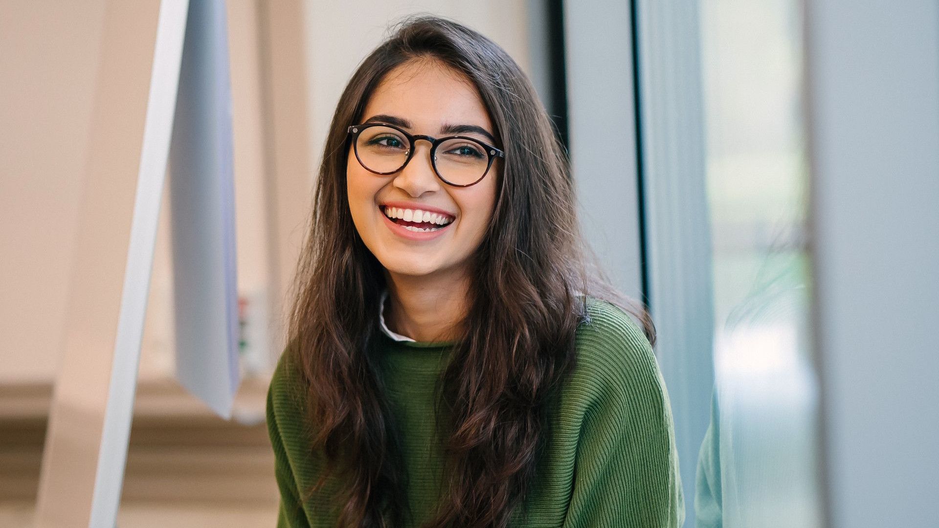 A smiling girl in a green sweater and wearing glasses.
