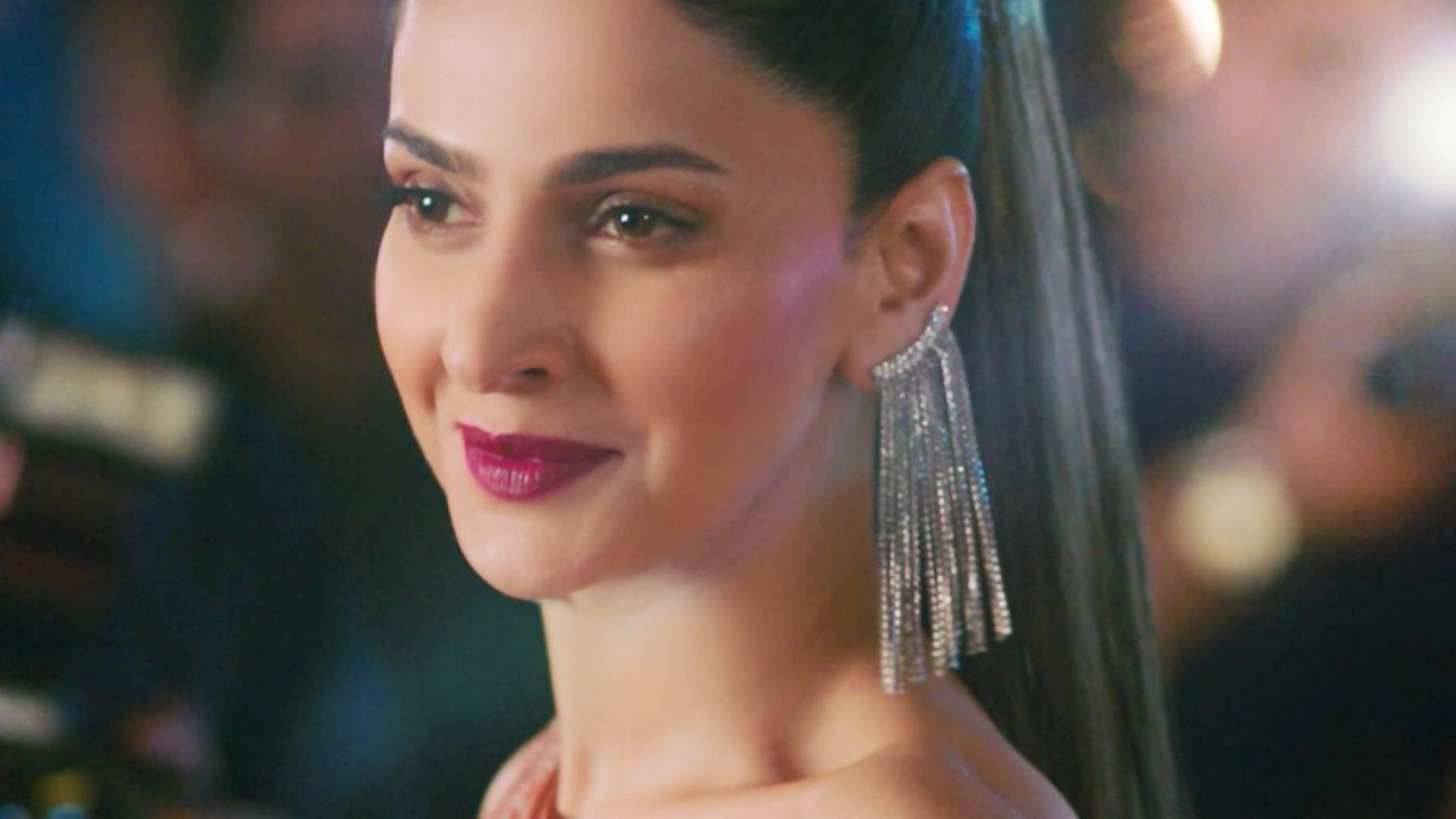 Close-up of a woman wearing long, silver, dangling earrings with straight dark hair pulled back in a sleek style.