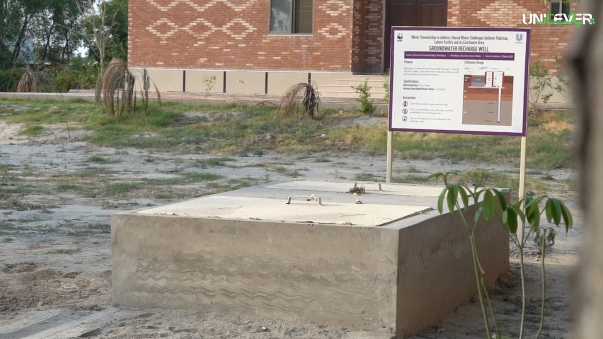 Concrete groundwater recharge well structure in a yard beside a brick building with an information sign
