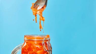 A stream of water splashes into a clear glass jar filled with green herbs and red and white striped beetroot slices.